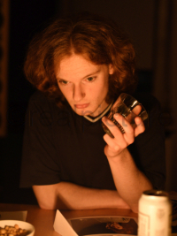 Ein Teenager ist nachdenklich und trinkt bei Kerzenlicht etwas.