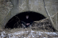 Ein Jugendlicher sitzt mit gespenstisch beleuchtetem Gesicht in einem dunklen Mauerbogen